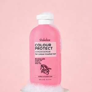 Pink Shakebar Colour Protect conditioner bottle for colour-treated hair with a white cap, set against a pale pink background with soap suds at the base.