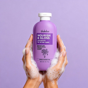 Purple Shakebar Nourish & Gloss Shampoo bottle held between soapy hands against a lavender background, with descriptive label text visible.