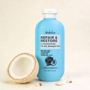 Blue bottle of Shakebar Repair & Restore conditioner for dry, damaged hair with a halved coconut beside it on a light background.