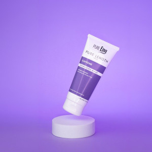 Purple background with a white and purple tube labeled 'Pure Envy Pure Length Caffeine Energizing Mask' resting on a white pedestal (cosmetic product).