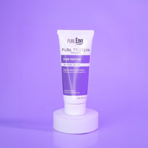 Tube of Pure Protein Intense Mask keratin treatment standing on a white circular pedestal against a lavender-purple background